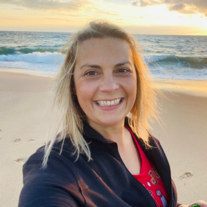 picture of a woman on a beach in sunset background smiling to the camera